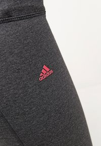 Grå träningsleggings med en slät yta och tajt passform, med en rosa Adidas-logotyp på låret.
