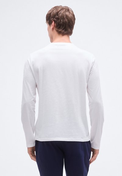 Hvit langermet skjorte laget av mykt stoff, med rund hals og avslappet passform. Synlige sømmer ved kant og mansjetter.