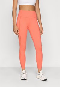 Leggings de cintura alta en un brillante color coral, fabricados con una tela elástica. Presentan costuras laterales y una silueta ajustada con una textura suave.