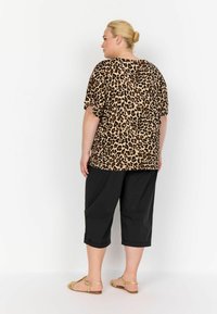 Tričko s leopardím potiskem a krátkými rukávy, spárované s černými zkrácenými kalhotami. Sandály mají tkané pásky. Hladká textura a volný střih.