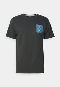 Camiseta de color gris oscuro con mangas cortas, que presenta un gráfico geométrico turquesa en el lado izquierdo del pecho. Material de algodón suave y diseño de cuello redondo.