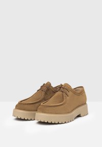 Scarpe in suede marrone con lacci, punta arrotondata, suola spessa beige e dettagli di cucitura visibili. Progettate per durevolezza e comfort.