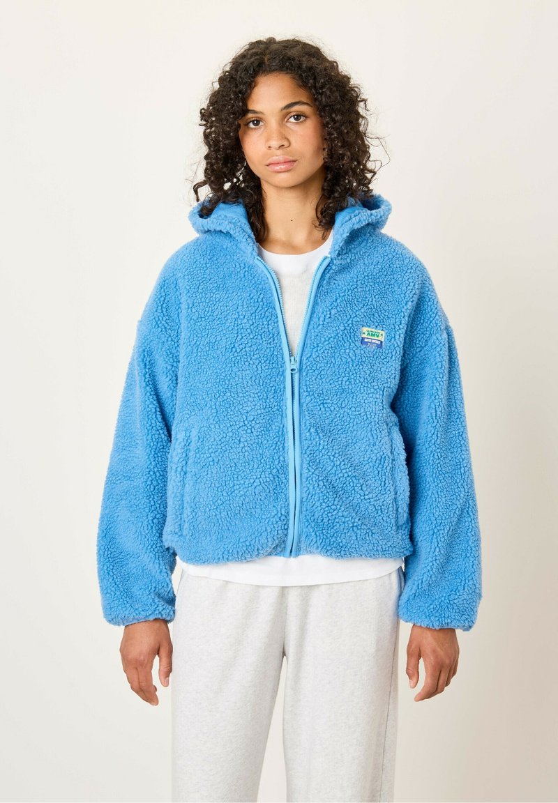 Blauwe fleecejack met een zachte, gestructureerde oppervlakte, capuchon en een voorrits. Heeft zijzakken en een klein logopatch op de borst.