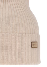 Cappello beanie a coste beige con risvolto e una piccola etichetta rettangolare marrone chiaro cucita sul risvolto.