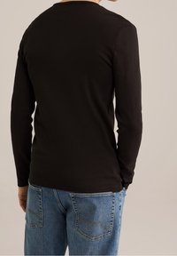 Svart långärmad T-shirt sedd bakifrån, gjord av bomull, med rund halsringning och figursydda ärmar, kombinerad med blåjeans.