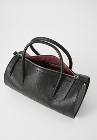 Black textured leather handbag with two handles, zip closure, and a red interior lining. Features smooth hardware details and streamlined shape.