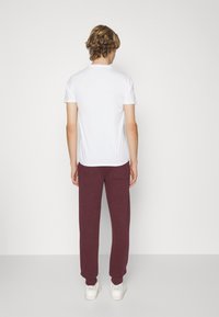 White short-sleeve t-shirt paired with burgundy sweatpants. T-shirt has a round neckline; sweatpants feature a back pocket and cuffed hems.