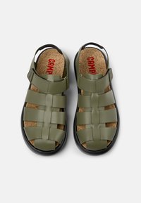 Olivi vihreät sandaalit, joissa on kudottu muotoilu, valmistettu sileästä materiaalista, sisältäen korkkipohjan, säädettävän hihnan ja mustan kumipohjan.