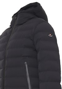 Piumino nero con collo alto, chiusura con zip sul davanti e una toppa con logo sulla manica sinistra. Dettagli in cucitura testurizzata su tutta la superficie.
