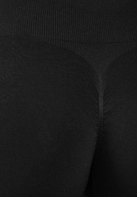 Gros plan sur un tissu côtelé noir montrant la couture et la texture d'un vêtement, probablement des leggings ou des collants, avec une taille haute.