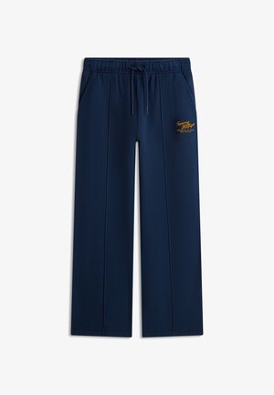 Granatowe szerokie spodnie dresowe z elastycznym pasem, sznurkiem do regulacji, bocznymi kieszeniami, przednimi szwami oraz małym żółtym logo Tommy Hilfiger na lewej udzie.