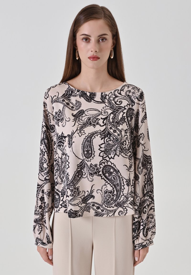 Blusa a maniche lunghe in tessuto rosa chiaro con motivo paisley nero. Collo arrotondato e vestibilità ampia, con polsini arricciati sulle maniche.