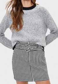 Šedý textured pletený svetr s kulatým výstřihem, doplněný černobílou kostkovanou minisukní s páskem a předními kapsami.