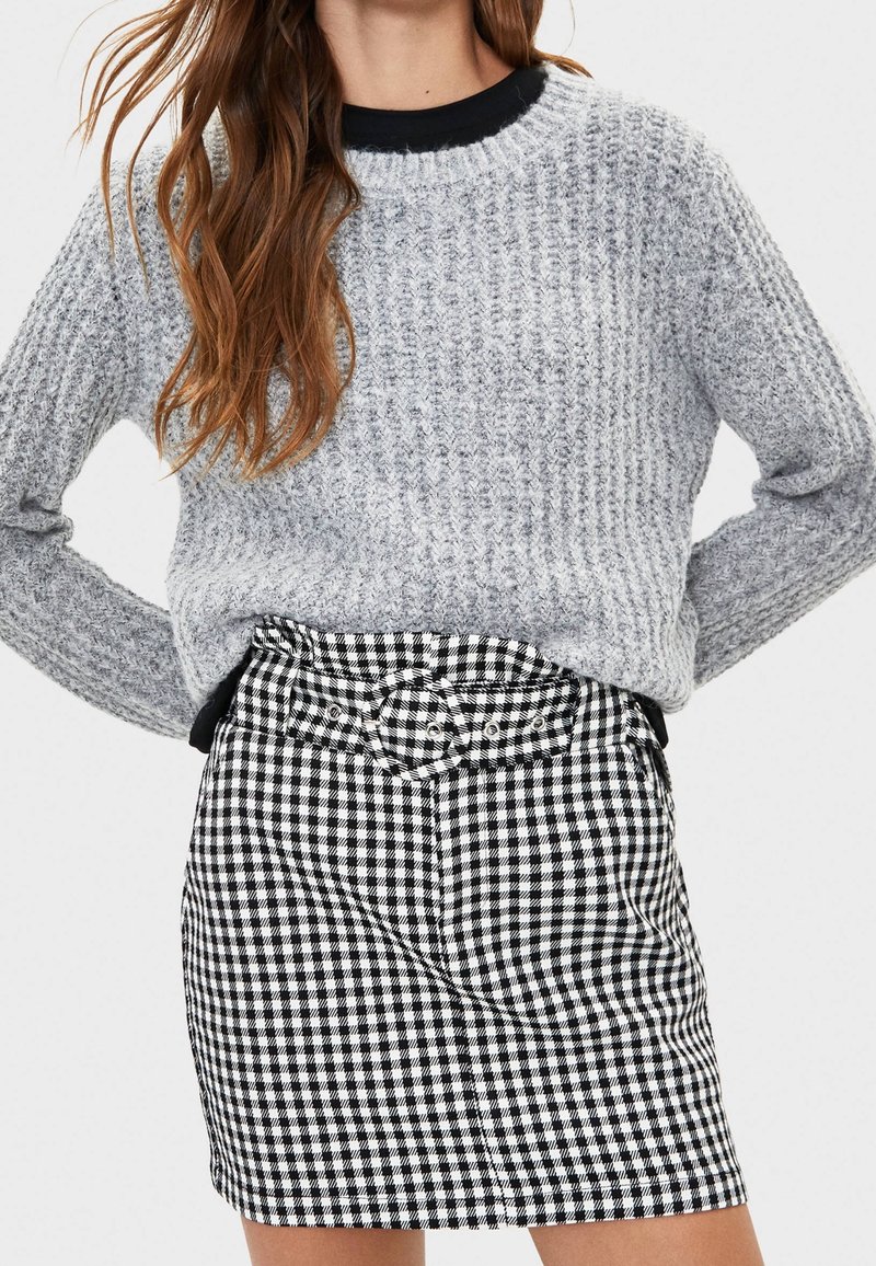 Šedý textured pletený svetr s kulatým výstřihem, doplněný černobílou kostkovanou minisukní s páskem a předními kapsami.