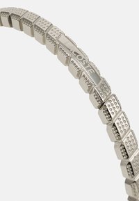 Il braccialetto in metallo presenta un design geometrico con sezioni alternate lisce e testurizzate, rifinito in argento con marchio in rilievo.