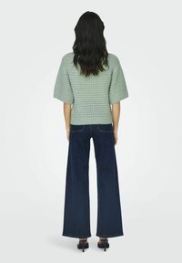 Ljusgrön stickad topp med lös passform och korta ärmar, kombinerad med mörkblå vida jeans. Slät textur med öppen vävstruktur.