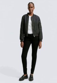 Crna kviltana bomber jakna s zatvaračem, nosi se preko bijele košulje. Uparena s crnim uskim trapericama i crnim platformama.