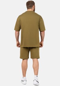 Set di camicia a maniche corte e shorts di colore verde oliva, realizzato in tessuto morbido, con una vestibilità relaxed e senza motivi visibili, abbinato a sneaker bianche.