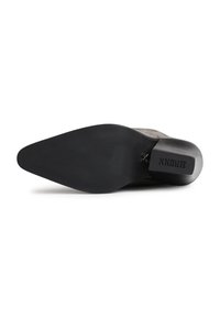 Semelle de chaussure avec une forme pointue, en caoutchouc noir, présentant une surface texturée et un logo en relief sur le talon.