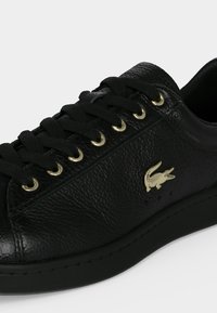 Baskets en cuir noir avec lacets noirs, œillets dorés et petit logo crocodile doré sur le côté.