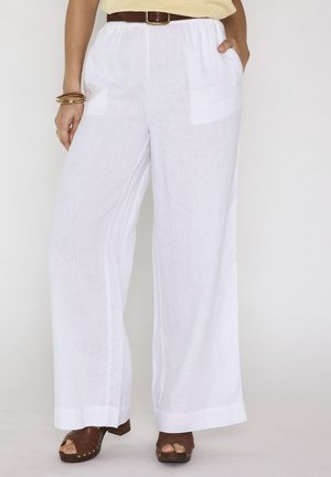 Femme portant un pantalon blanc à jambes larges avec poches latérales, une ceinture marron, un haut beige, des sandales à plateforme marron et des bracelets dorés.