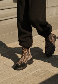 Stivaletti alla caviglia con stampa leopardata e suola nera spessa, realizzati in materiale liscio e con dettaglio della cerniera laterale, abbinati a pantaloni neri.
