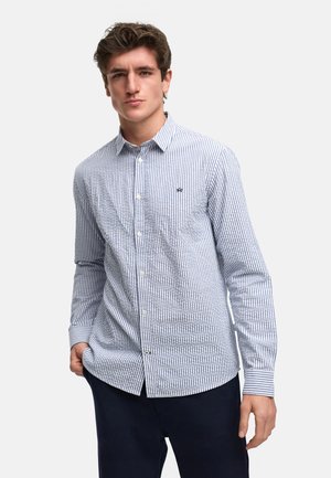 Camisa de botones de rayas azules y blancas, de material de algodón, con cuello puntiagudo y mangas largas. Cuenta con un logotipo bordado en el pecho.