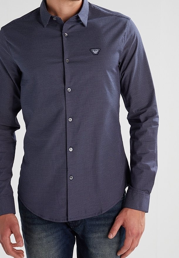 Chemise boutonnée bleu marine avec un petit patch logo, tissu texturé présentant un motif géométrique subtil, et manches longues.