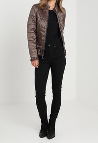 Brązowa pikowana kurtka bombka z stójką, z zamkiem błyskawicznym i falbaniastym dołem, zestawiona z czarnymi wąskimi dżinsami i botkami za kostkę.