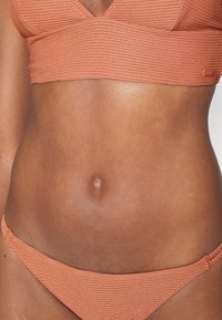 Hladký bikiny top a spodok z terakoty. Tkanina má textúrovaný vzor s lesklými akcentmi. Na oboch kusoch sú nastaviteľné ramienka.