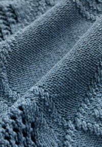 Material tricotat într-o nuanță albastru moale și estompat, cu modele texturate și cusături delicate. Aspect neted și ușor elastic.