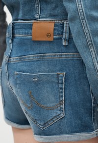 Κοντινό πλάνο σε πίσω μέρος μπλε τζιν σορτς με διπλωμένο στρίφωμα και ταμπέλα από καφέ δέρμα στη μέση.