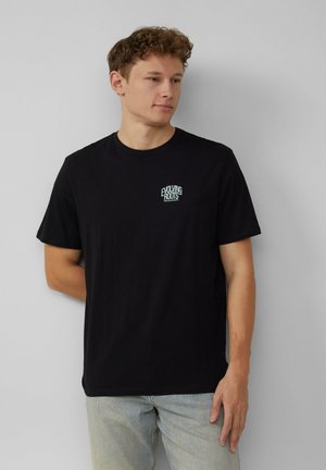 Zwarte katoenen t-shirt met een klein, turquoise "EVOLVING ROOTS" logo op de borst, met korte mouwen en een ronde hals.