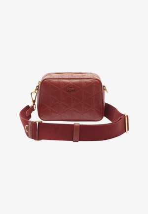 Sac bandoulière rectangulaire en cuir rouge avec motif embossé et logo crocodile, doté d'une large sangle en tissu réglable avec des éléments dorés.