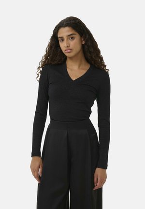 Schwarzes langärmliges Oberteil mit V-Ausschnitt, aus geripptem Material, kombiniert mit hochtaillierten schwarzen Hosen mit Falten-Design.