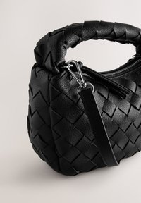 Sac à main en cuir tressé noir avec poignée tressée, fermeture éclair et bandoulière amovible ; présente une surface texturée et des accents en métal.