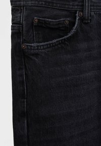 Gros plan sur la poche avant et le passant de ceinture d’un jean en denim foncé, montrant les coutures et les rivets métalliques sur le tissu.
