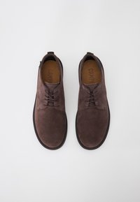 Chaussures en suede marron foncé à lacets avec des semelles noires, vues de dessus sur un fond blanc.