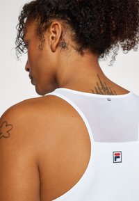 Valge sportlik tank top, mille seljal on silmapaistev võrkpaneel, keskel väike logo. Sile tekstuur ja ümmargune kaelus.
