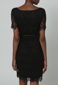 Czarna koronkowa sukienka z krótkimi rękawami, złożonymi wzorami kwiatowymi i falistymi, dopasowaną talią oraz falbaniastym dołem, z zamkiem błyskawicznym z tyłu.