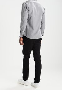 Camisa gris de manga larga con una textura sutil y puños abotonados, combinada con pantalones negros ajustados y zapatillas blancas. Diseño limpio y moderno.