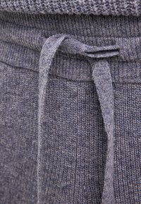 Szary dzianinowy materiał z teksturowanym wzorem, z wiązanym sznurkiem w pasie. Tkanina wydaje się miękka i przytulna.