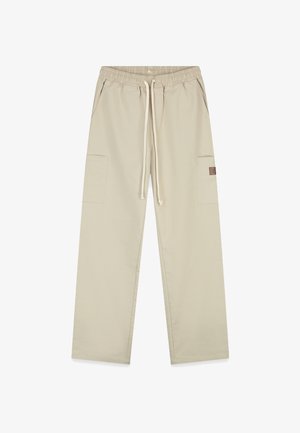 Beige cargobroek met een elastische tailleband, trekkoord, twee zijzakken en textuurstof; heeft een klein bruin logopatch op de bovenbeen.