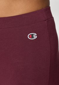 Maroon puuvillased sportpantsid, millel on elastne vöökoht ja väike punases, valges ja mustas värvitoonis tikand puusal.