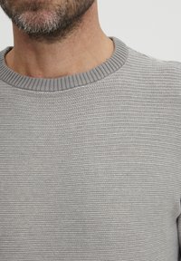 Maglione a maglia grigio chiaro con colletto rotondo a coste e motivo orizzontale testurizzato. La vista ravvicinata mette in evidenza i dettagli del tessuto.