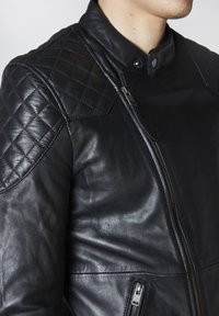 Svart skinnjacka med quiltat axeldesign, dragkedjestängning och sidofickor, med en mjuk textur och figurnära passform.