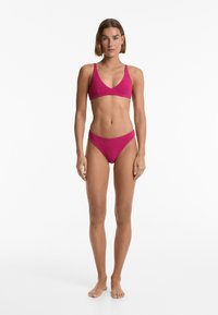 Fuchsiová bikiny souprava se strukturovanou tkaninou; trojúhelníková podprsenka s nastavitelnými ramínky a odpovídajícími nízkými kalhotkami.