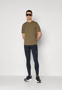 Vyšninės žalios spalvos marškinėliai, tamsiai mėlynos tamprės ir juodi sportbačiai, kuriuos dėvi vyras. Jis dėvi tamsius akinius nuo saulės ir turi tatuiruotę ant dešinės rankos.