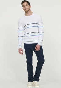 Witte gestreepte trui met roze, zwarte en blauwe lijnen, gecombineerd met marineblauwe broek en lichtgekleurde sneakers. Losse pasvorm en ribgebreide boorden.