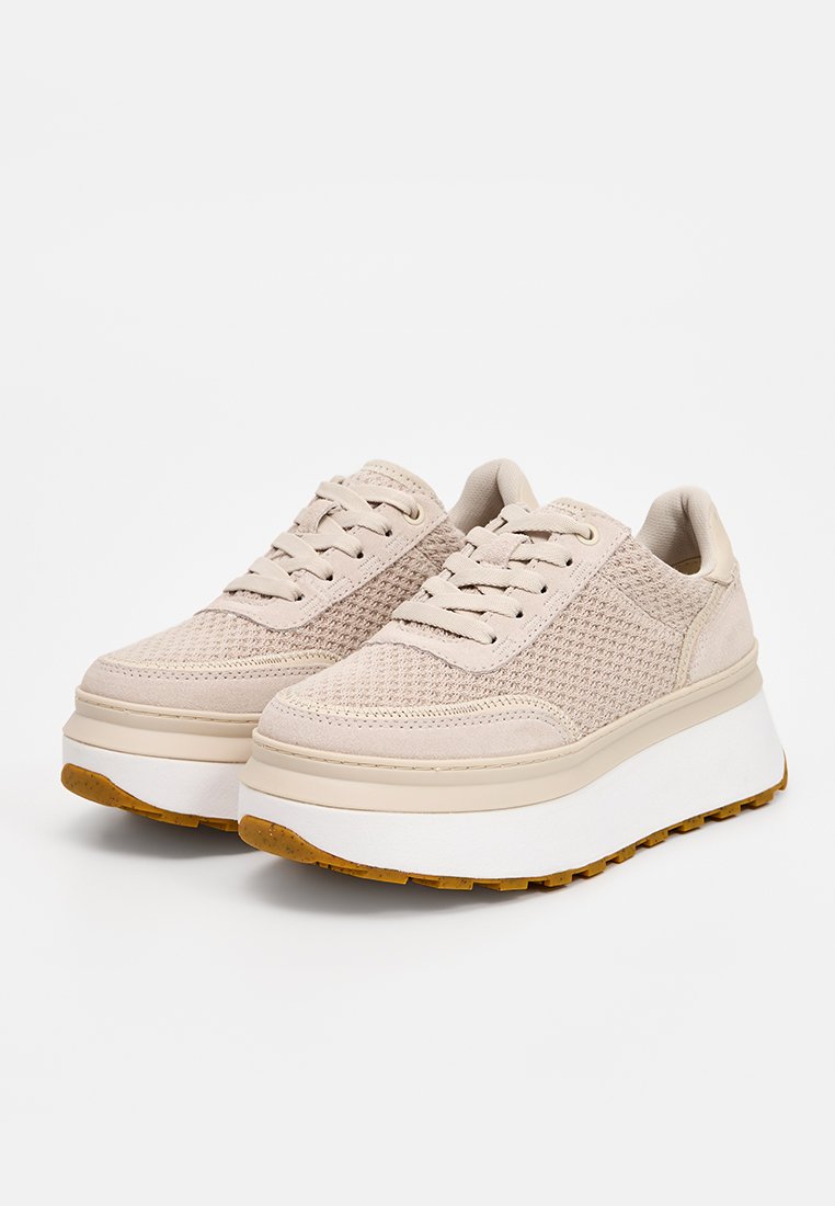 Beige Plattform-Sneaker mit strukturiertem Mesh-Obermaterial, Schnürdesign und einer dicken weißen Sohle, die mit einer braunen Gummisohle akzentuiert ist.